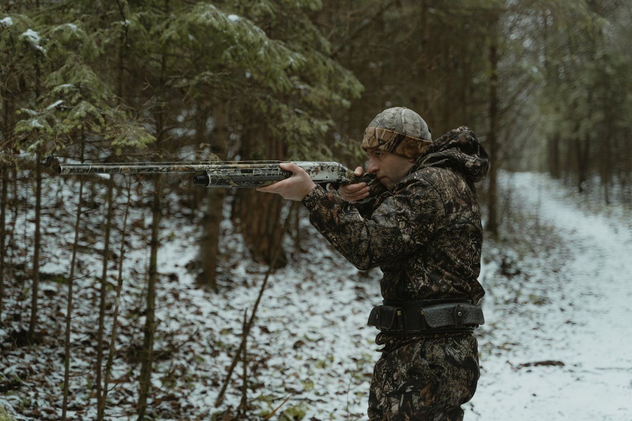 A man in the woods aiming and preparing to shoot.